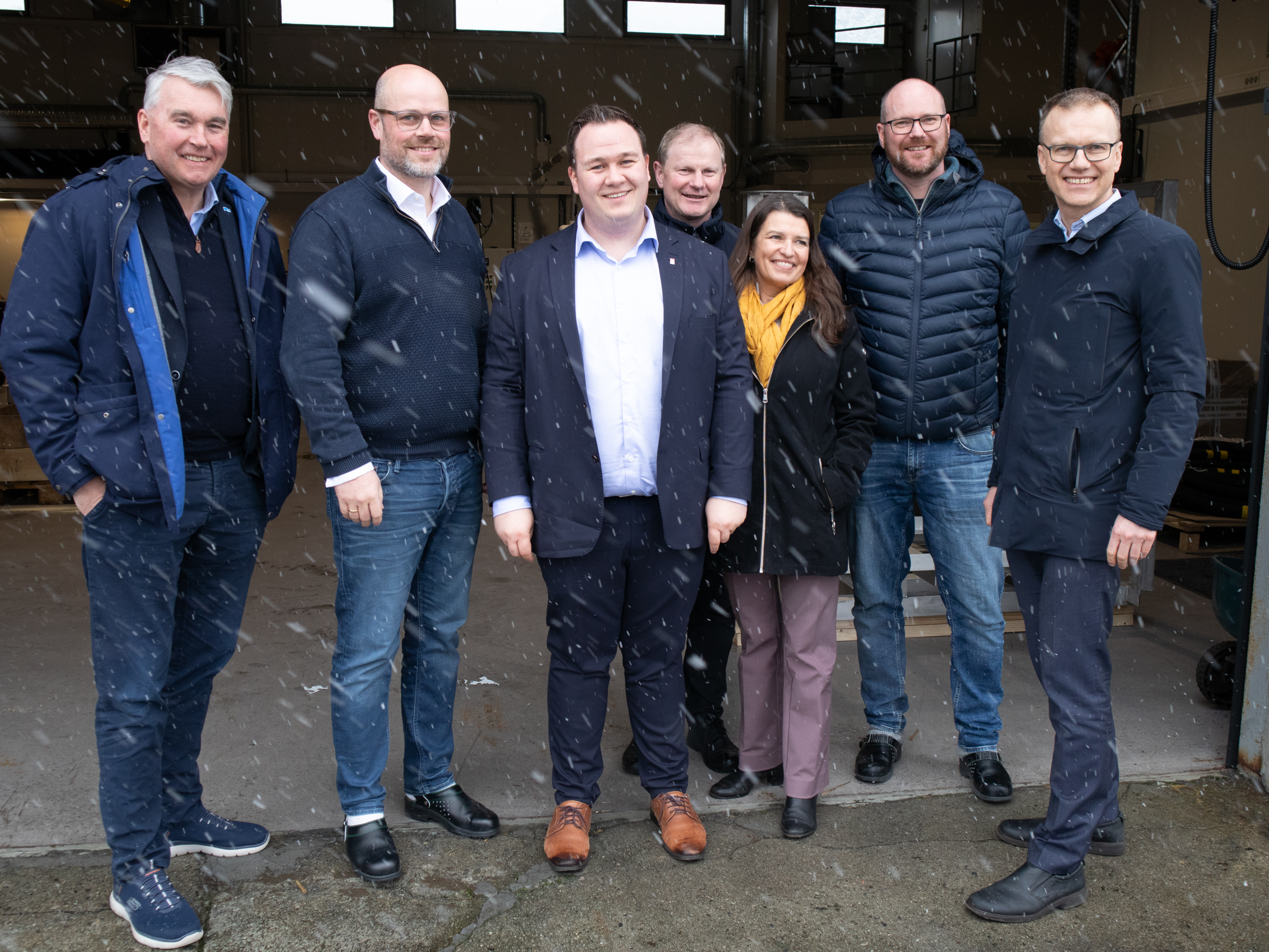 Medan snøen lava ned utanfor, søkte gjester og vertskap ly i porten til Helifuel sitt produksjonslokale. F.v.  Trond Helleland, Robert Brandvik (Helifuel), ordførar André Mundal Haukås, Erlend Larsen, Liv Kari Eskeland, Eirik Undesdal (Helifuel) og Erik Lahnstein (NHO Luftfart).